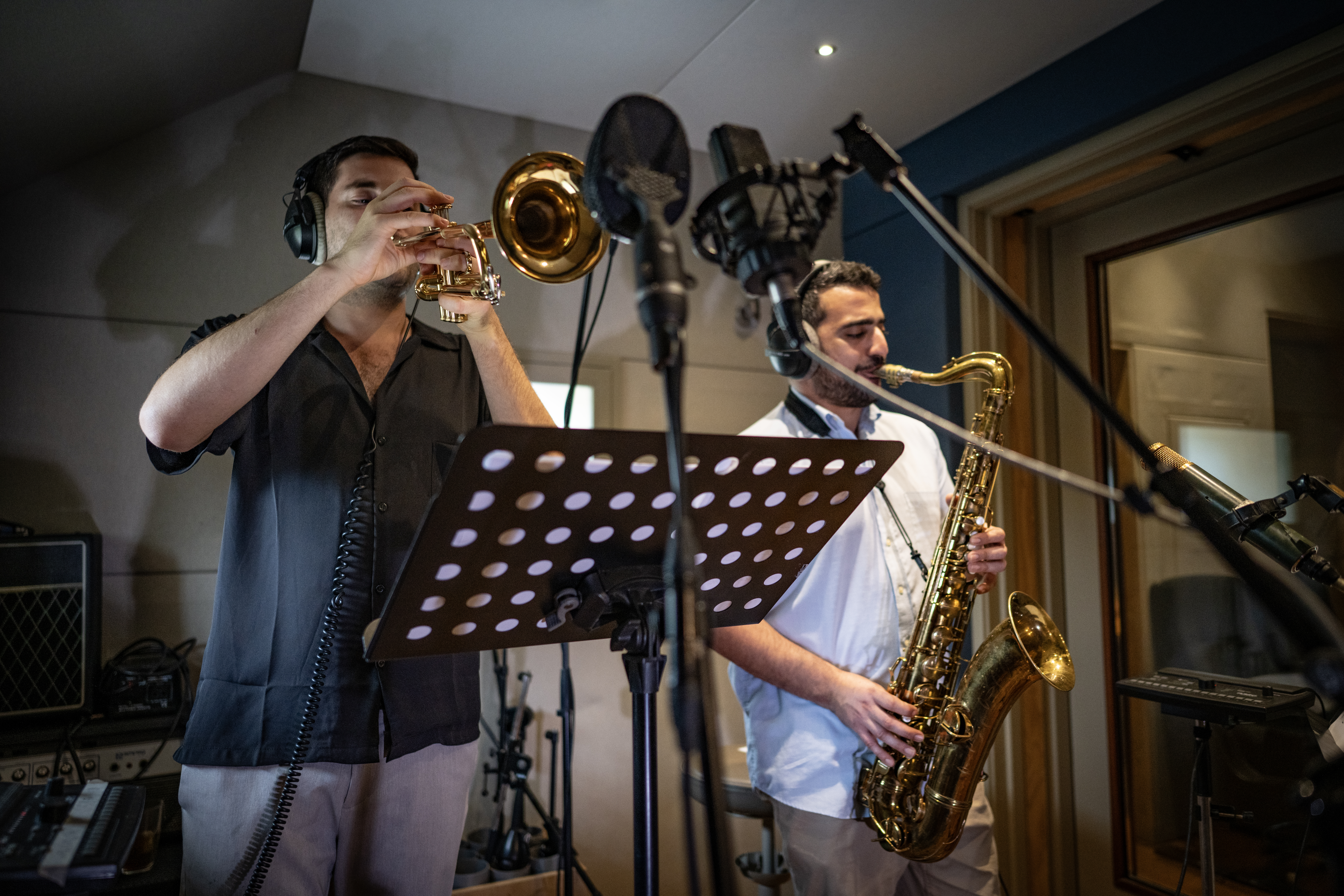 Trumpet and tenor saxophone players recording together at studio microphones.