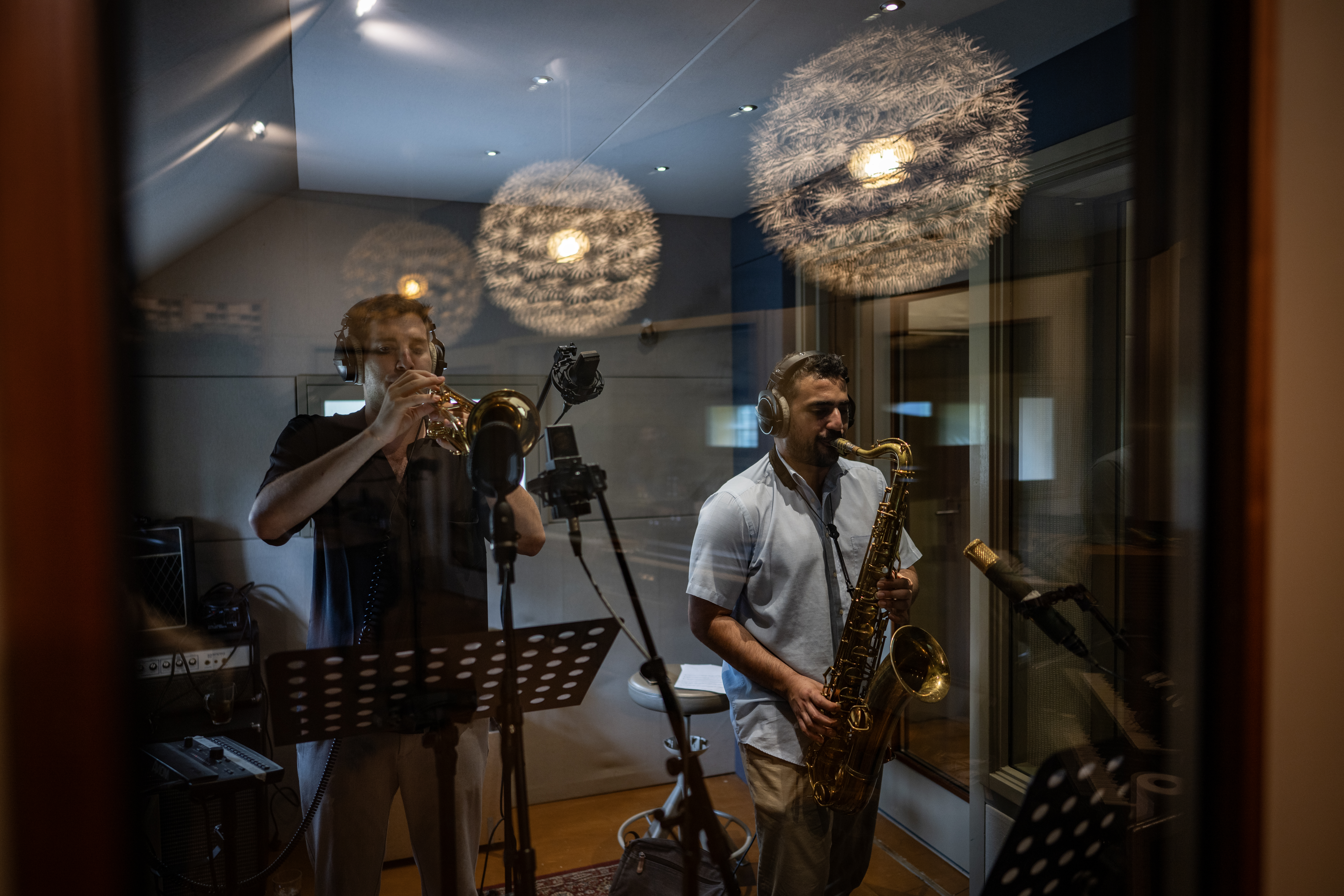 Trumpet and tenor saxophone recording, seen through the studio window.
