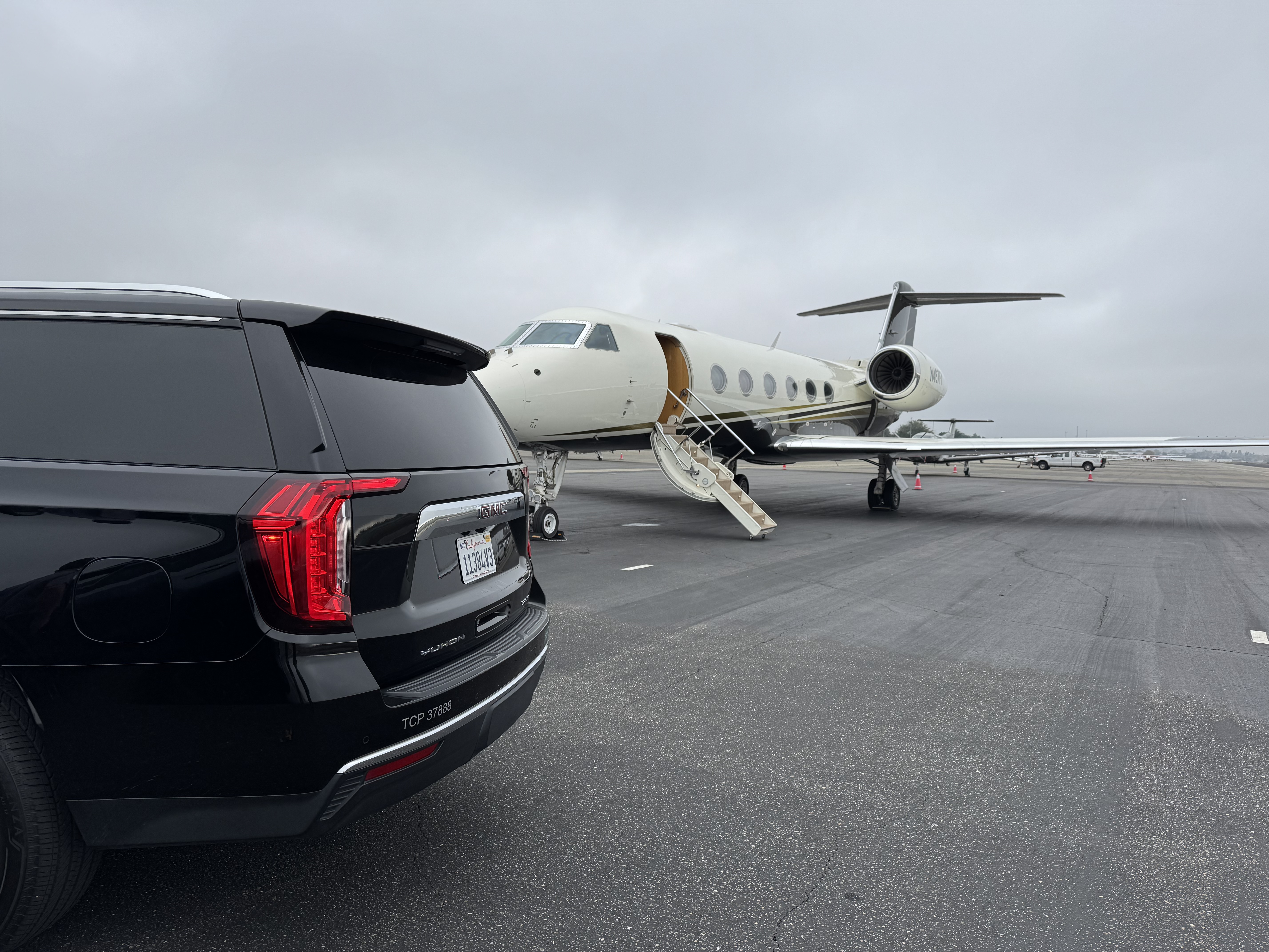 Black GMC Yukon SUV with TCP license waiting on tarmac beside a private jet at the FBO