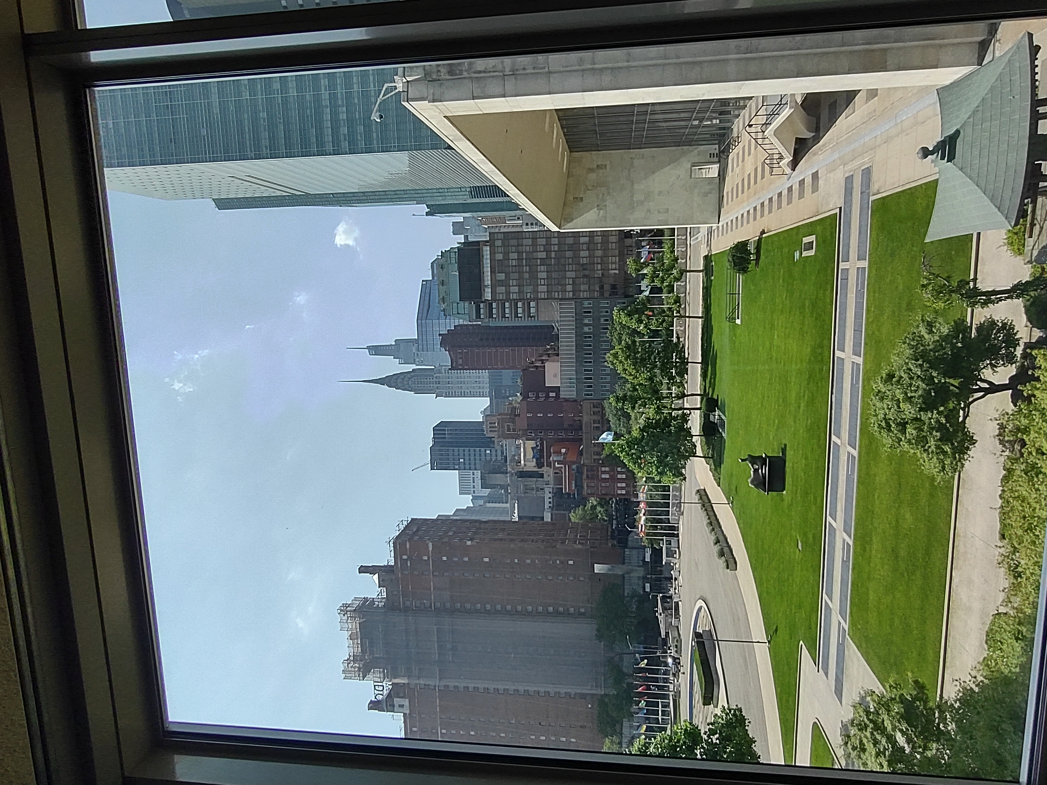 Manhattan skyline viewed through a window overlooking a green courtyard with the Chrysler Building
