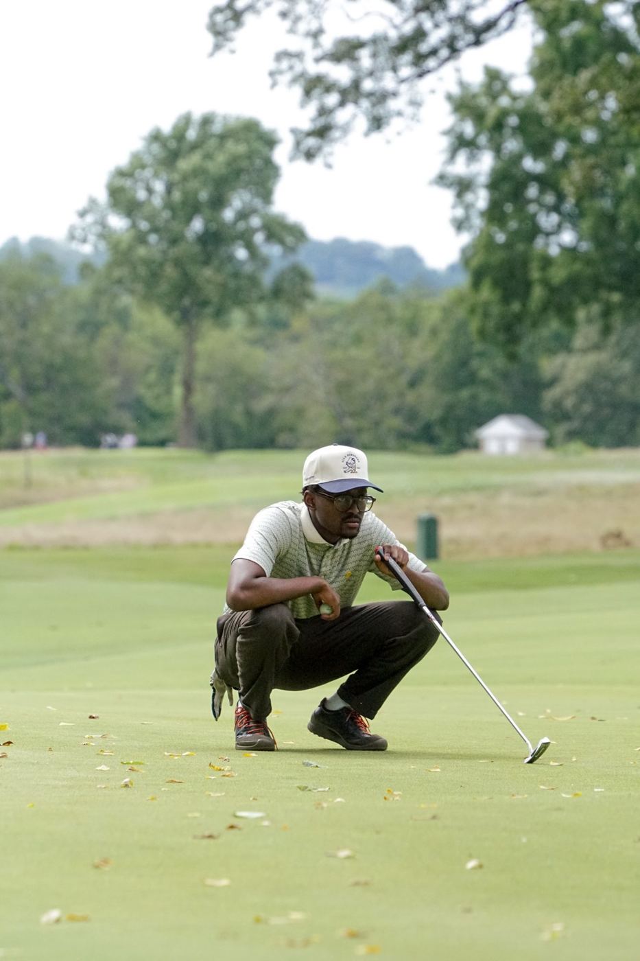 Member in an FBGC hat crouching to read a putt