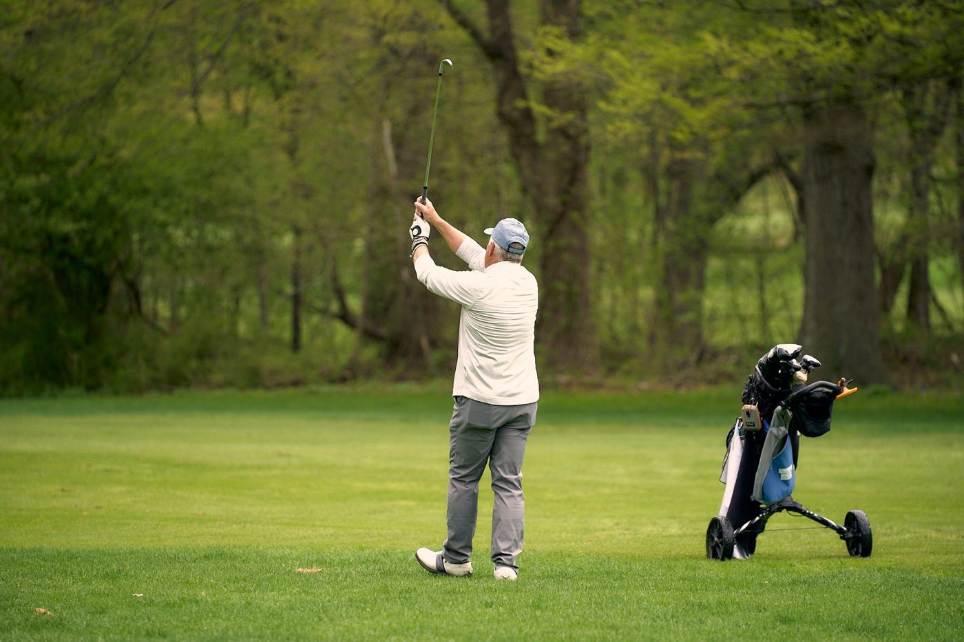 Member holding his finish after a tee shot, push cart beside him