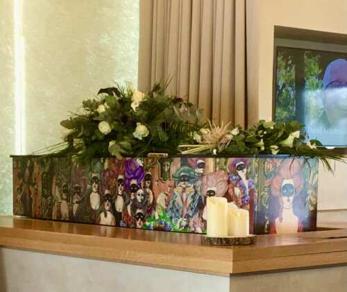 Personalised coffin with flowers and candles in a memorial setting.