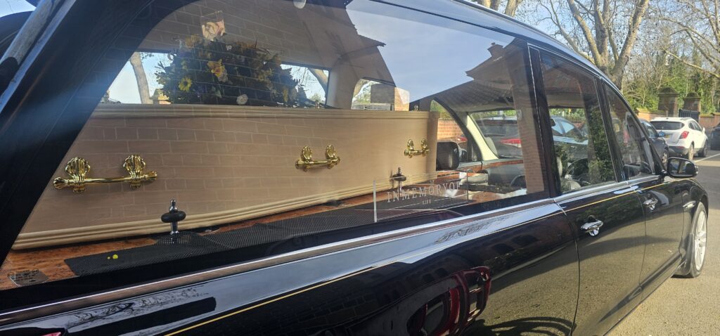 Coffin inside a hearse parked outside with floral arrangement.