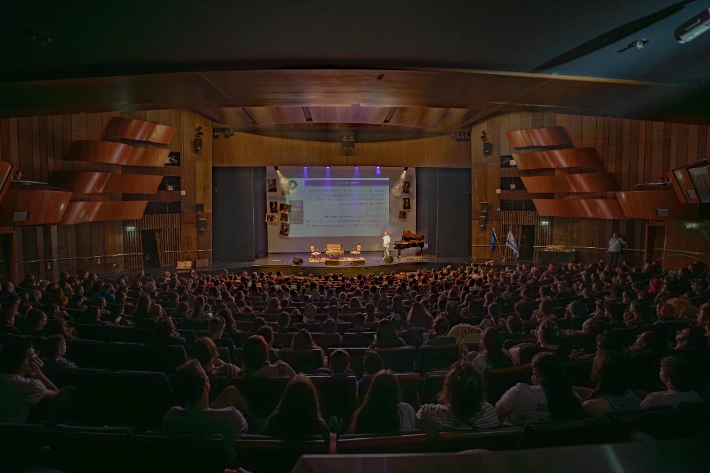 מרצה על הבמה מול קהל באירוע הוגיקון