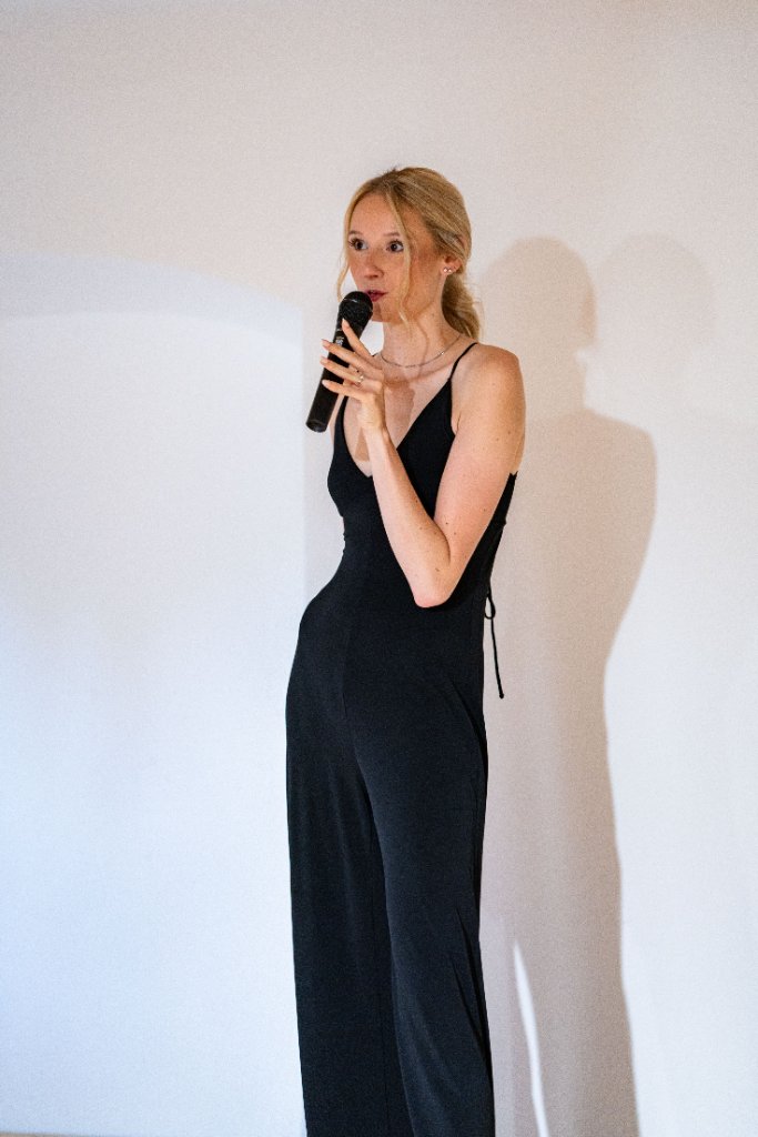 Opening , žena v černém overalu s mikrofonem