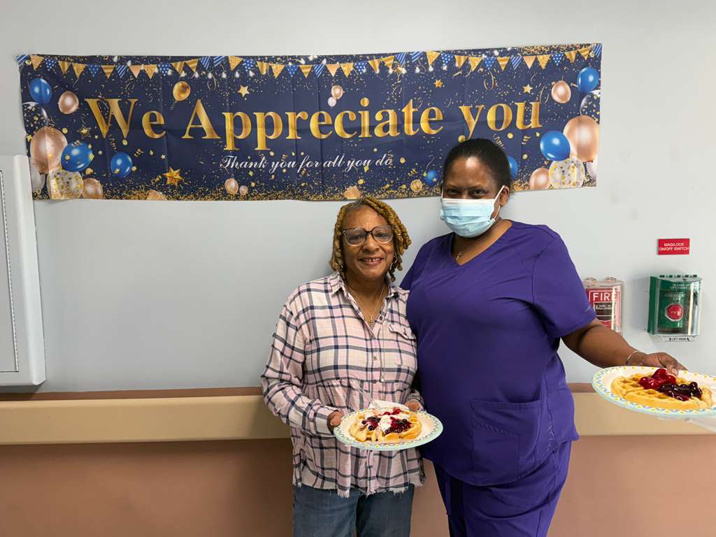 Two staff members posing with waffles at appreciation banner