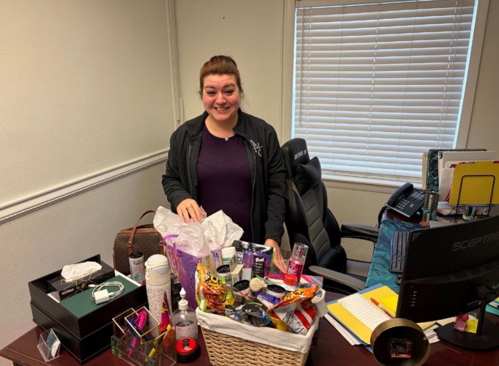 Administrator smiling behind a gift basket at her desk during Administrators Week.