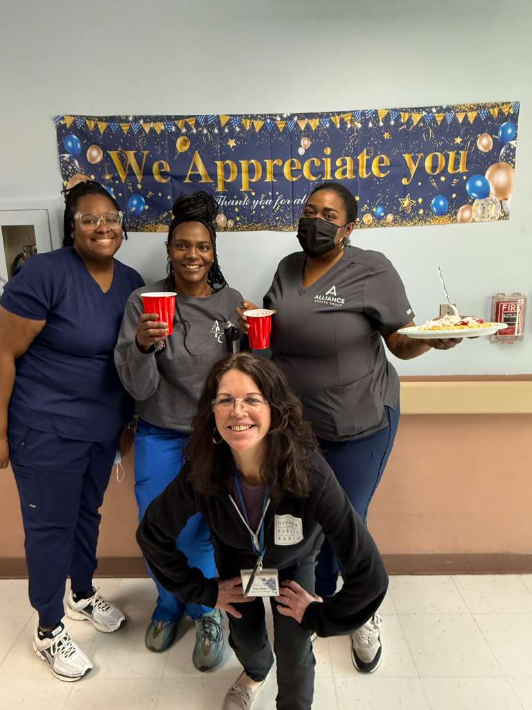 Group of staff members smiling in front of appreciation banner