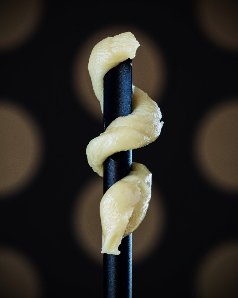 Creamy rosin wrapped around a black dab tool on a dark background