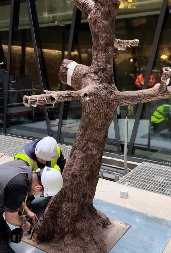 Two workers in hard hats and hi-vis vests working on a tree trunk on a construction site