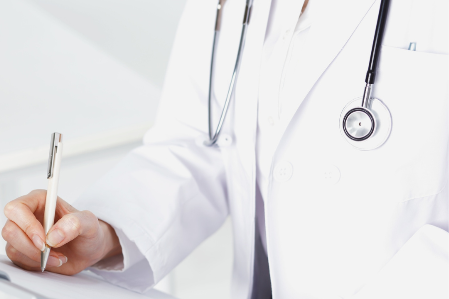 Doctor in white lab coat with stethoscope writing on a document