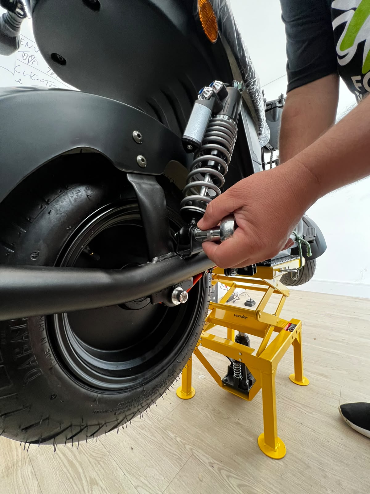 Técnico apertando parafuso da suspensão traseira com chave de catraca em scooter elétrica elevada