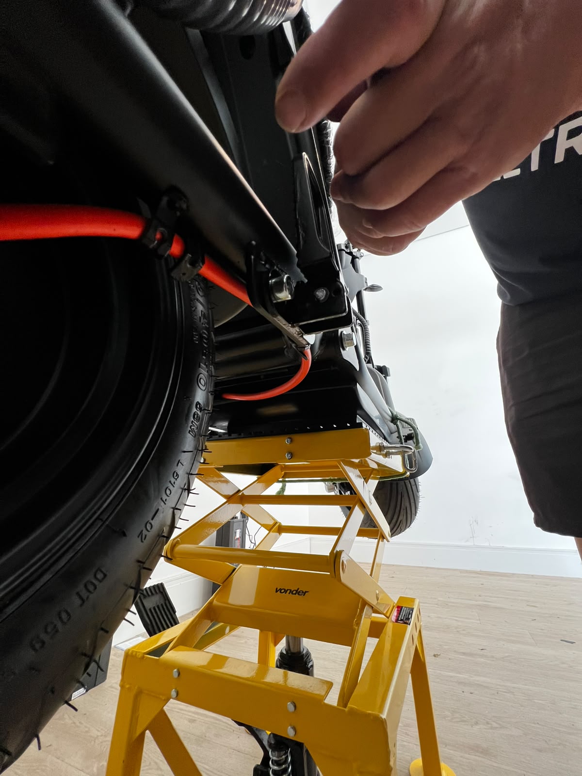 Ajuste da suspensão traseira de scooter elétrica com cabo laranja visível na oficina Four Eletric