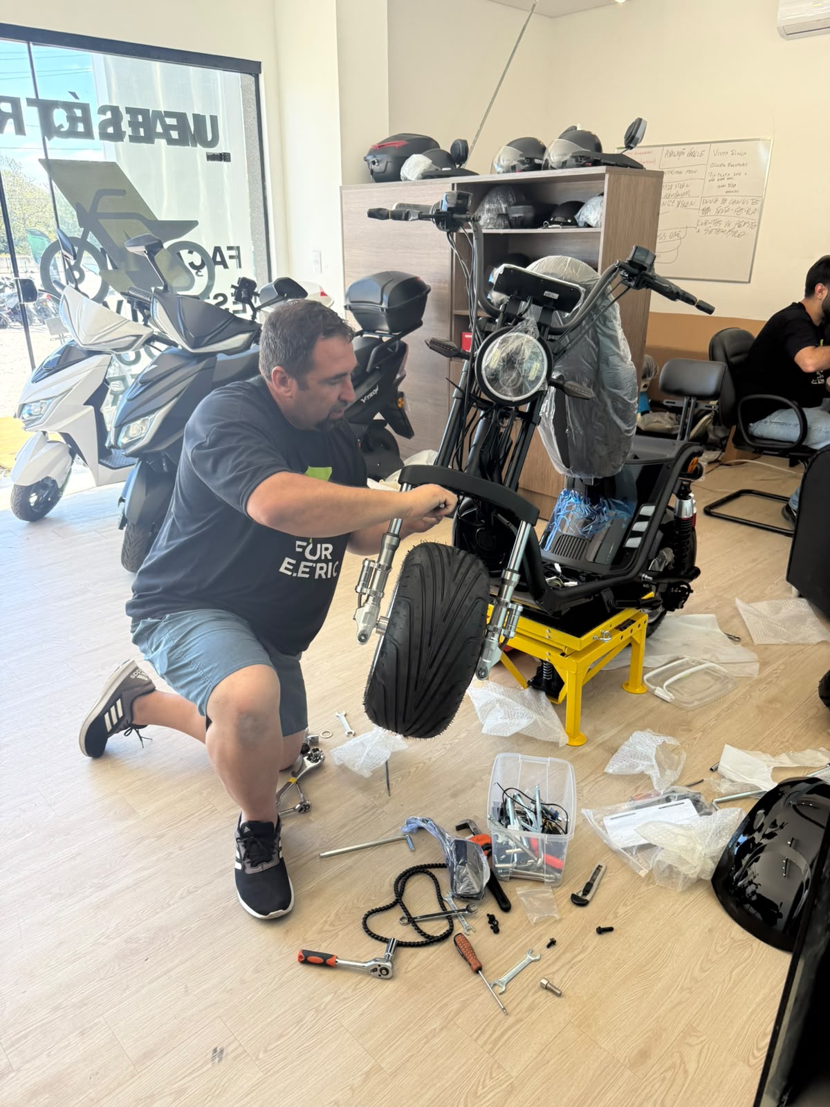 Técnico da Four Eletric montando e revisando uma scooter elétrica em oficina, com ferramentas e suporte