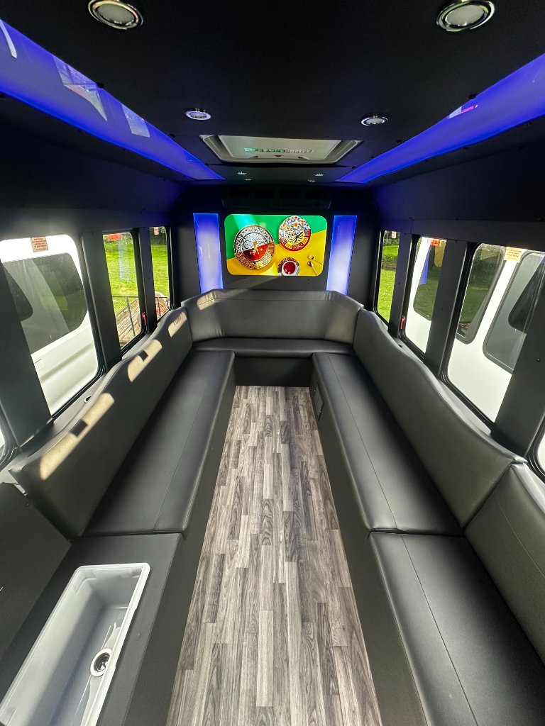 Inside the Greene Valley Shuttle party bus — black leather wraparound lounge seating, LED accent lighting, and hardwood floor.