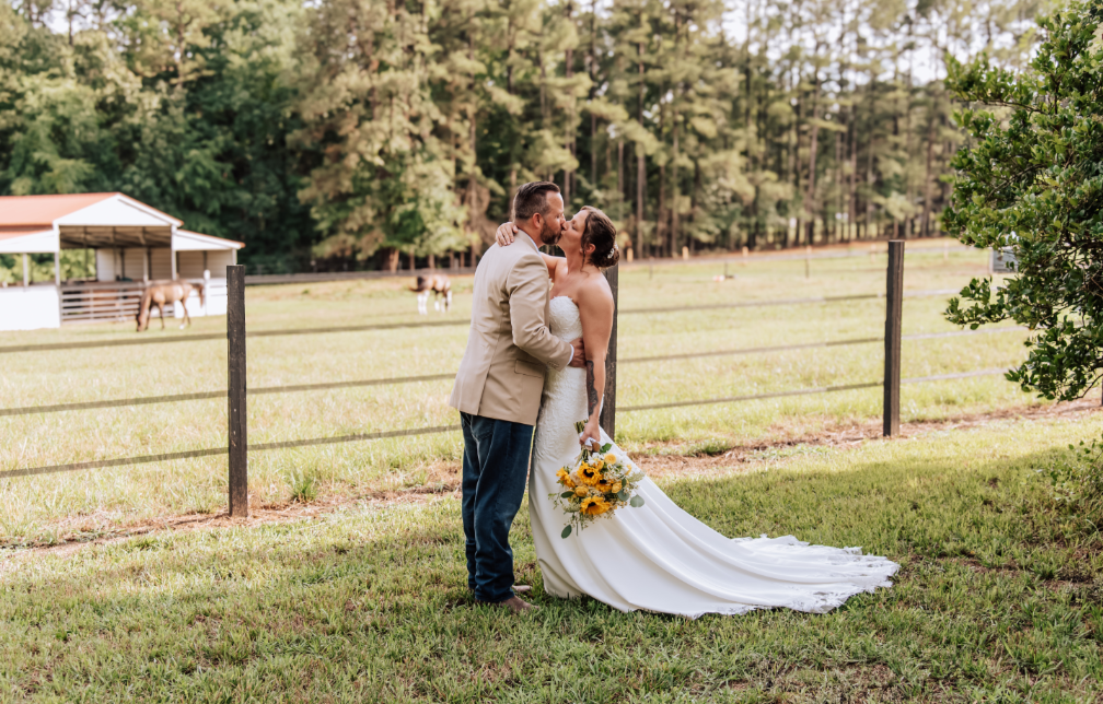 A sweet kiss by the pasture with horses nearby.