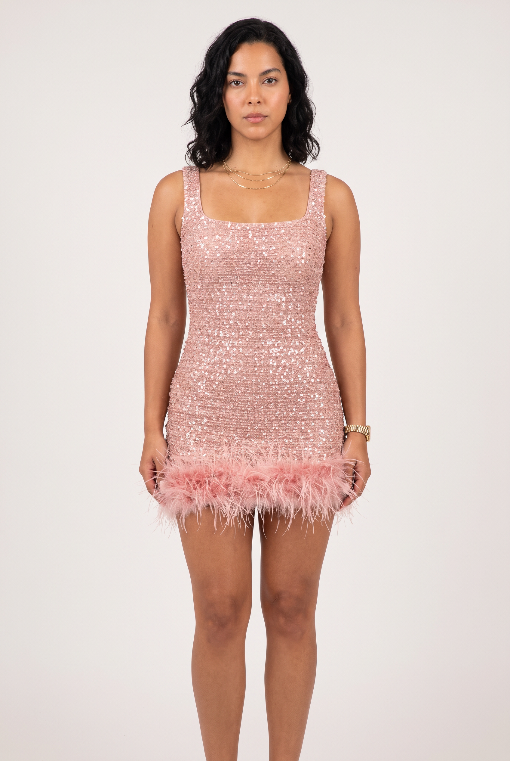 A woman wears a sleeveless pink sequin mini dress with a soft pink feather trim along the bottom hem.