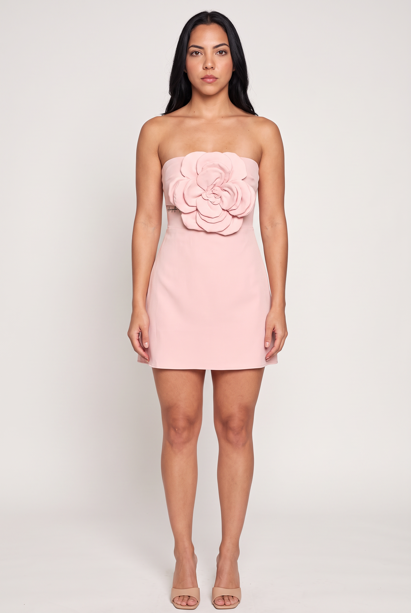 A woman wearing a pale pink strapless mini dress with a large sculpted floral accent on the bodice.