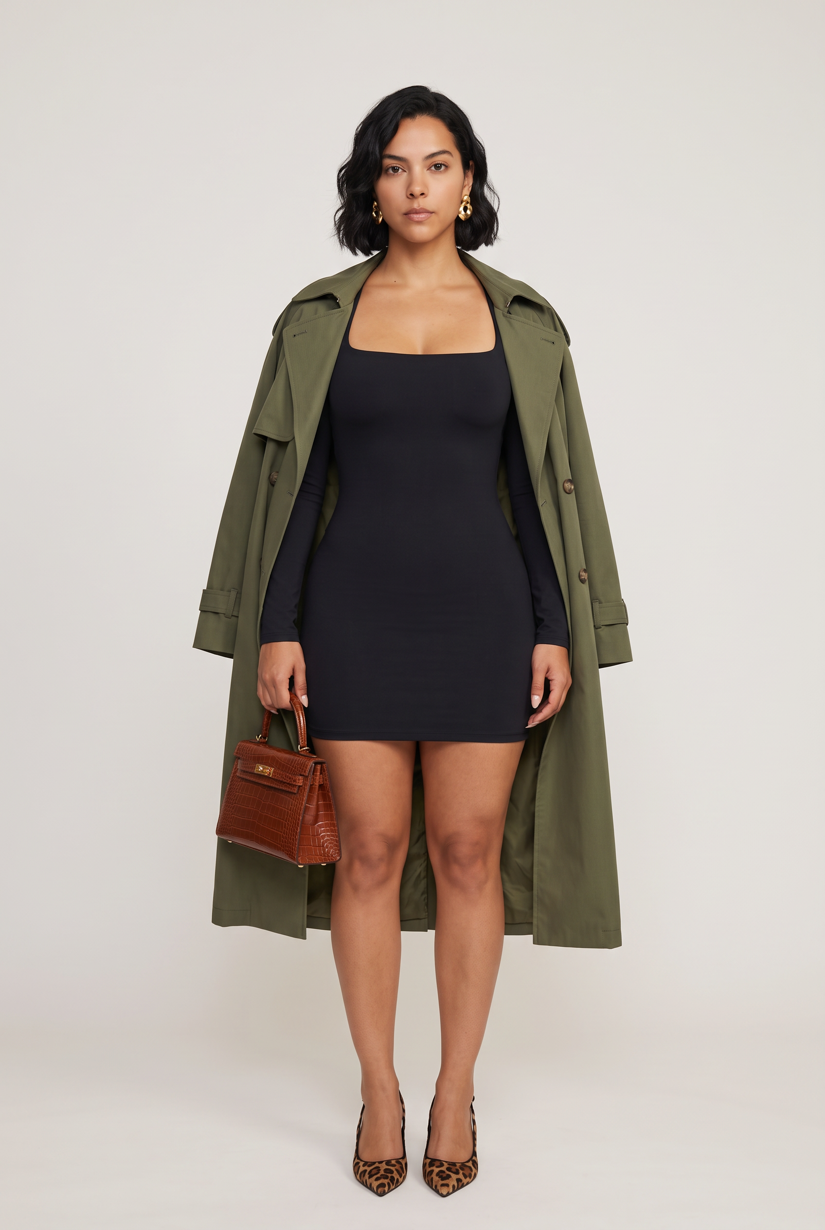 A woman wears a black long-sleeved mini dress layered under an olive green trench coat paired with a brown embossed handbag and leopard print heels.