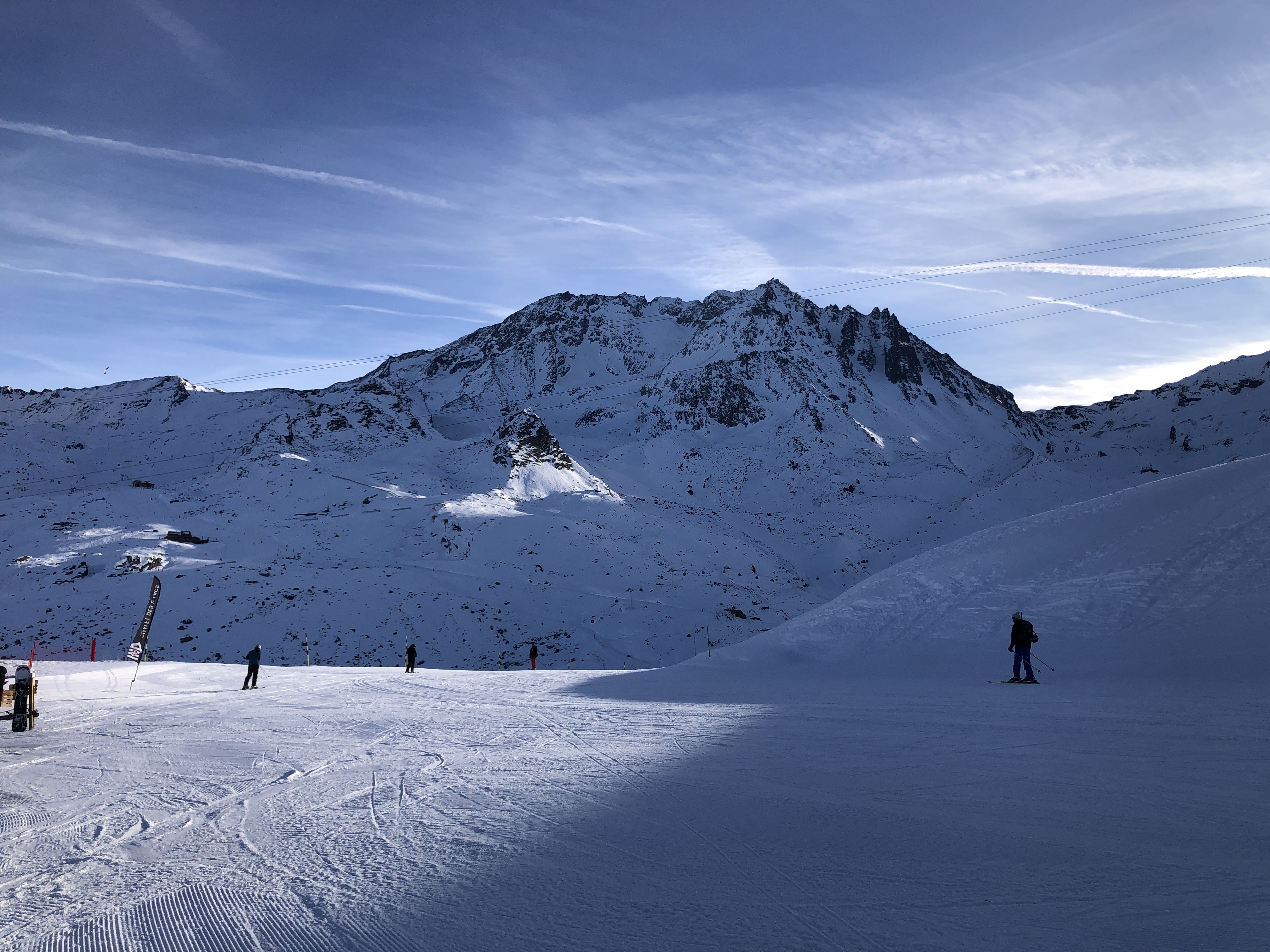 Skiers on a wide alpine snowfield beneath snow-capped peaks