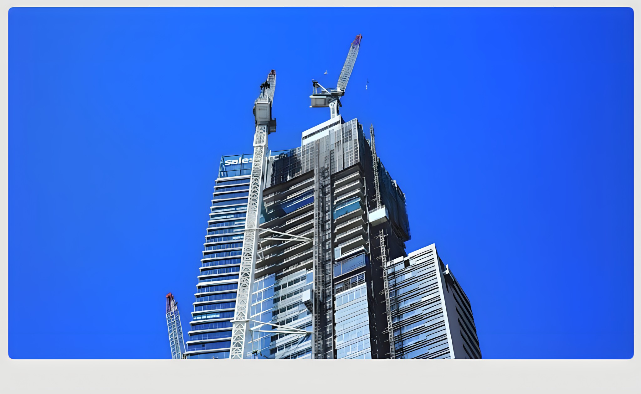 High-rise residential tower under construction with tower cranes against a blue sky