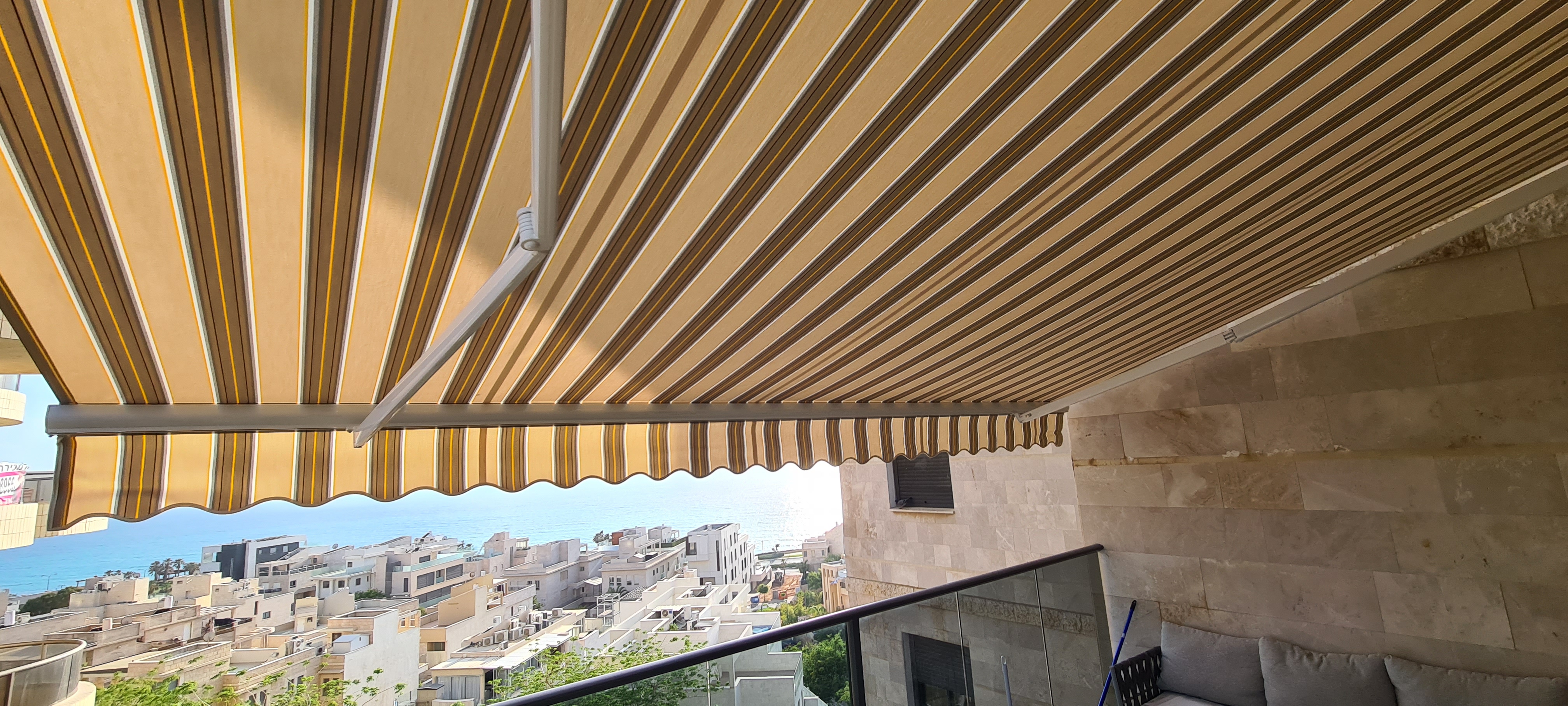 סוכך זרועות בפסי בז' וחום עם נוף לים — הצללה למרפסת מול קו החוף