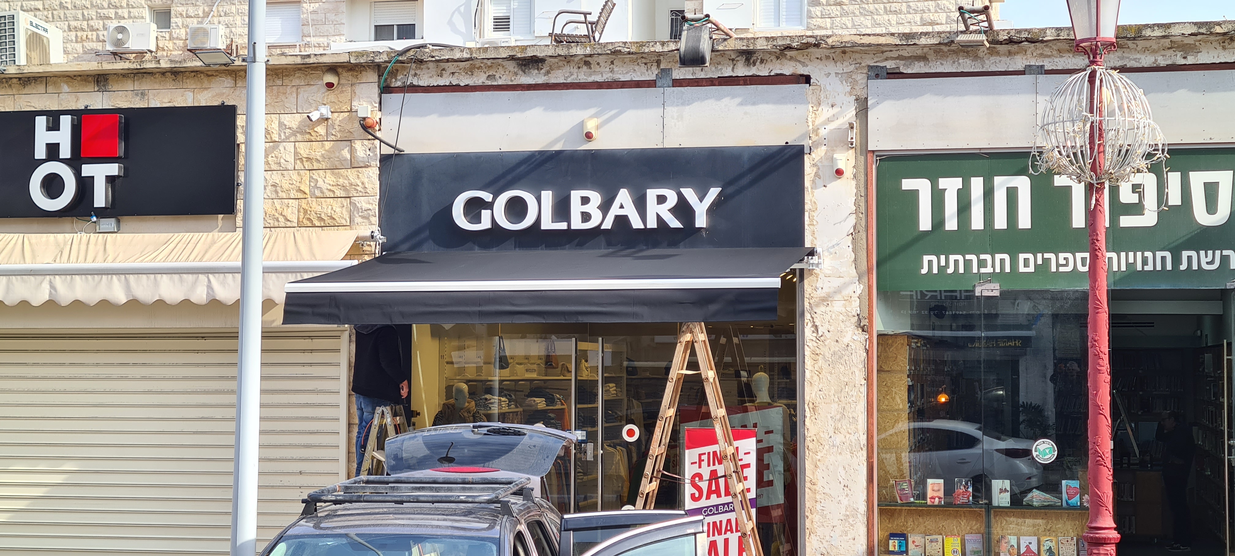 התקנת סוכך זרועות שחור לחנות GOLBARY — המתקין מרכיב את זרועות הסוכך בחזית העסק