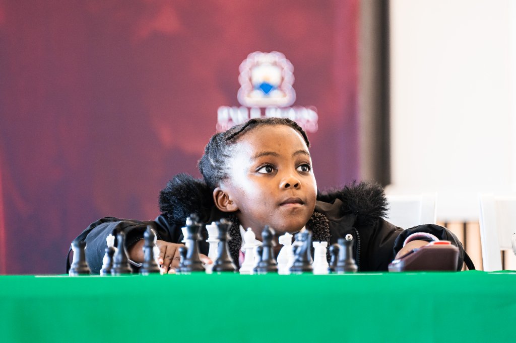 A young girl playing chess at an African Chess Lounge event, focused and contemplative