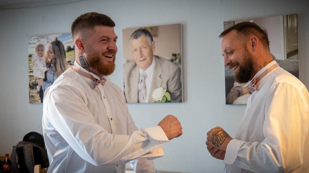 Two men in formal wedding attire laughing indoors