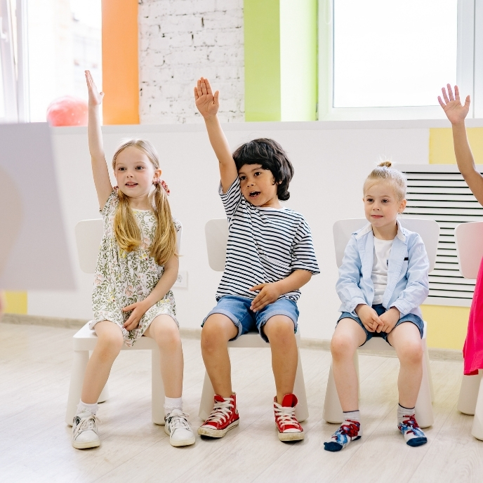 Young students raising their hands in a bright classroom during a Penny the Pelican financial literacy lesson