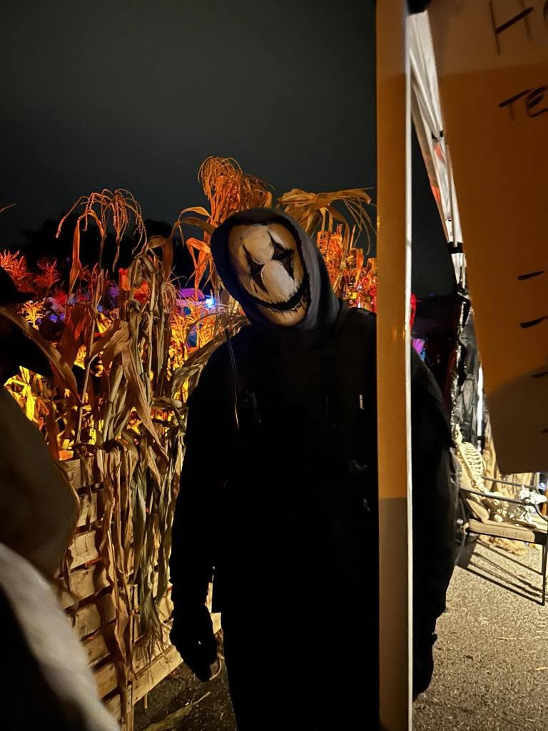 Costumed actor in a bone-white mask standing in front of corn stalks at Nightmare on Norwood
