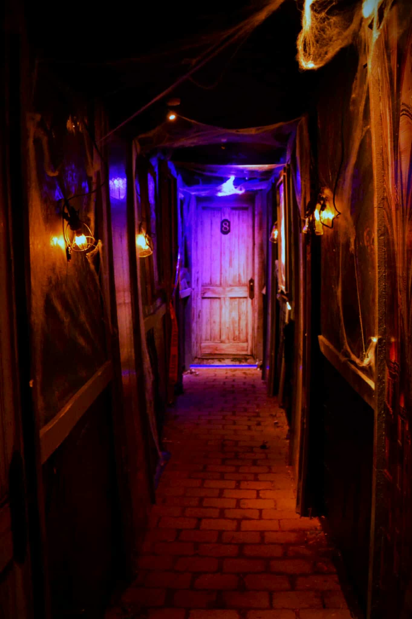 Dark haunted hallway at Nightmare on Norwood lit by amber sconces with violet light at the far door