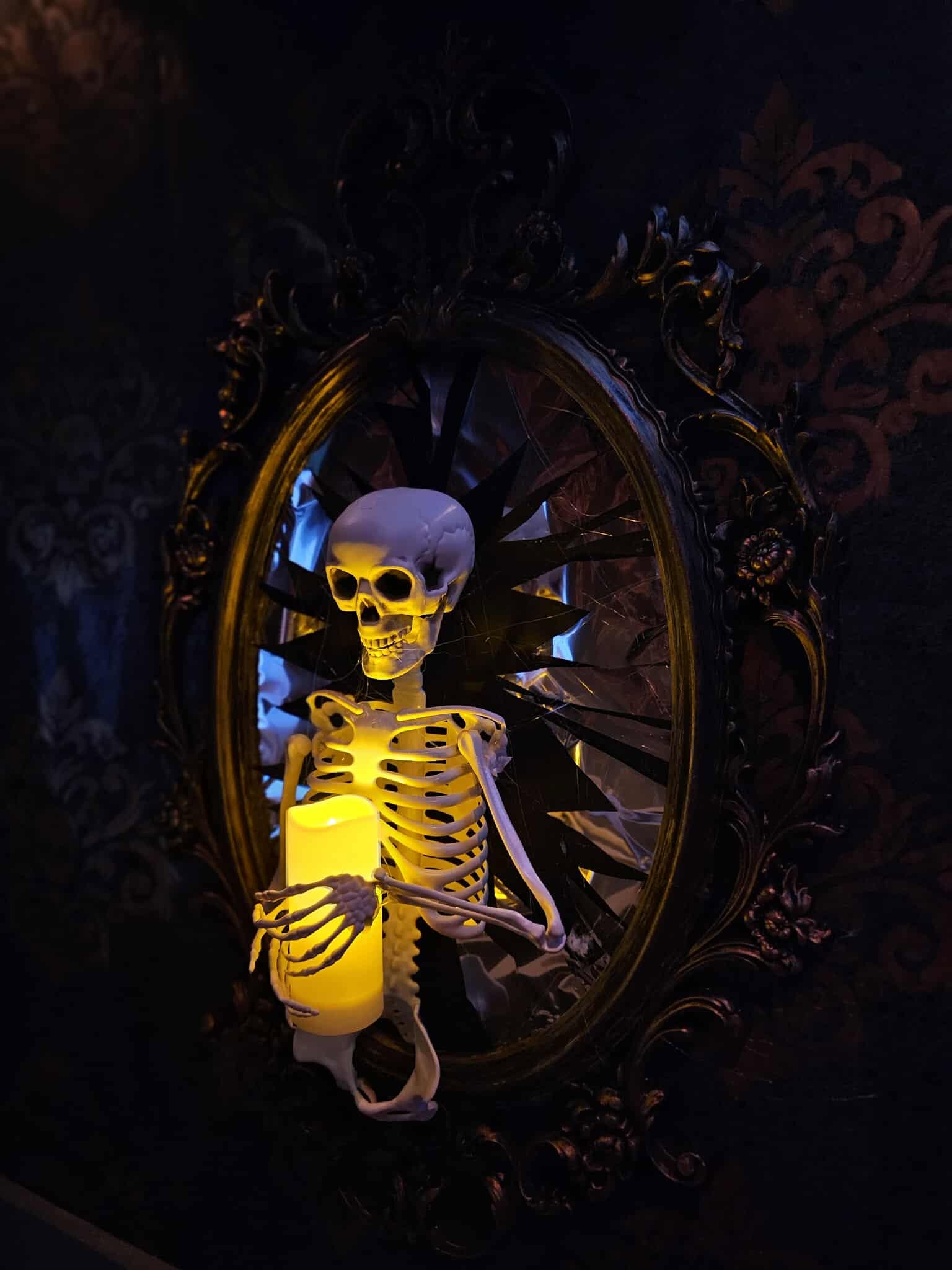 Skeleton prop holding a glowing candle in front of an antique mirror inside Nightmare on Norwood
