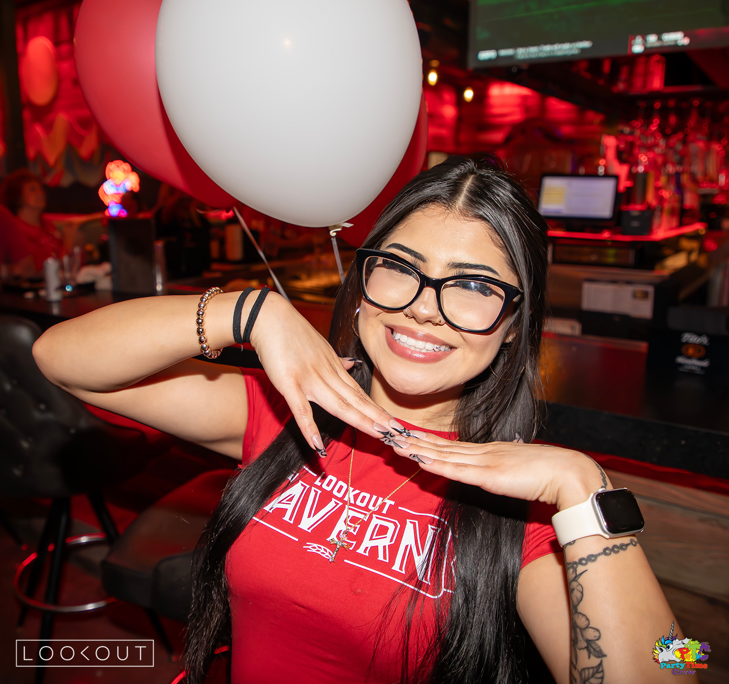 A server smiling under red and white game-day balloons at the bar