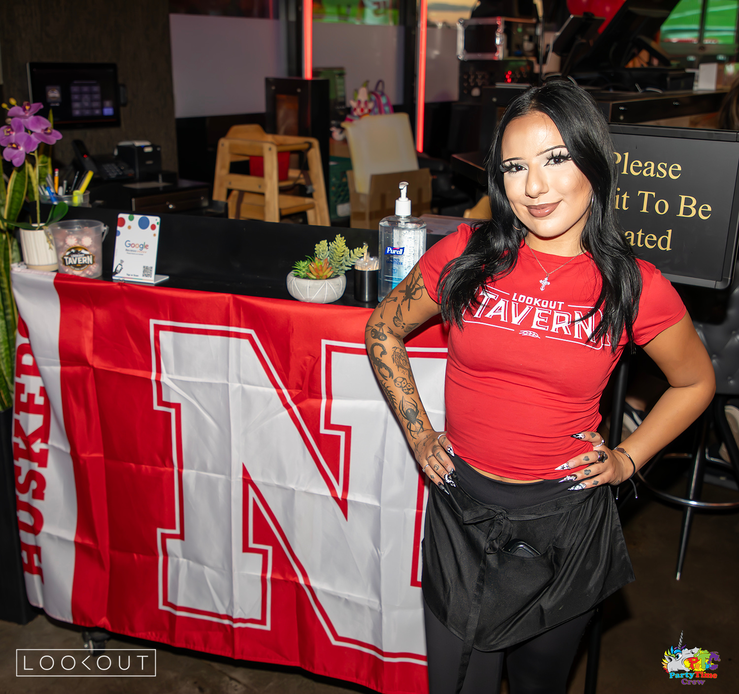 A Lookout Tavern server beside the Nebraska N flag at the host stand