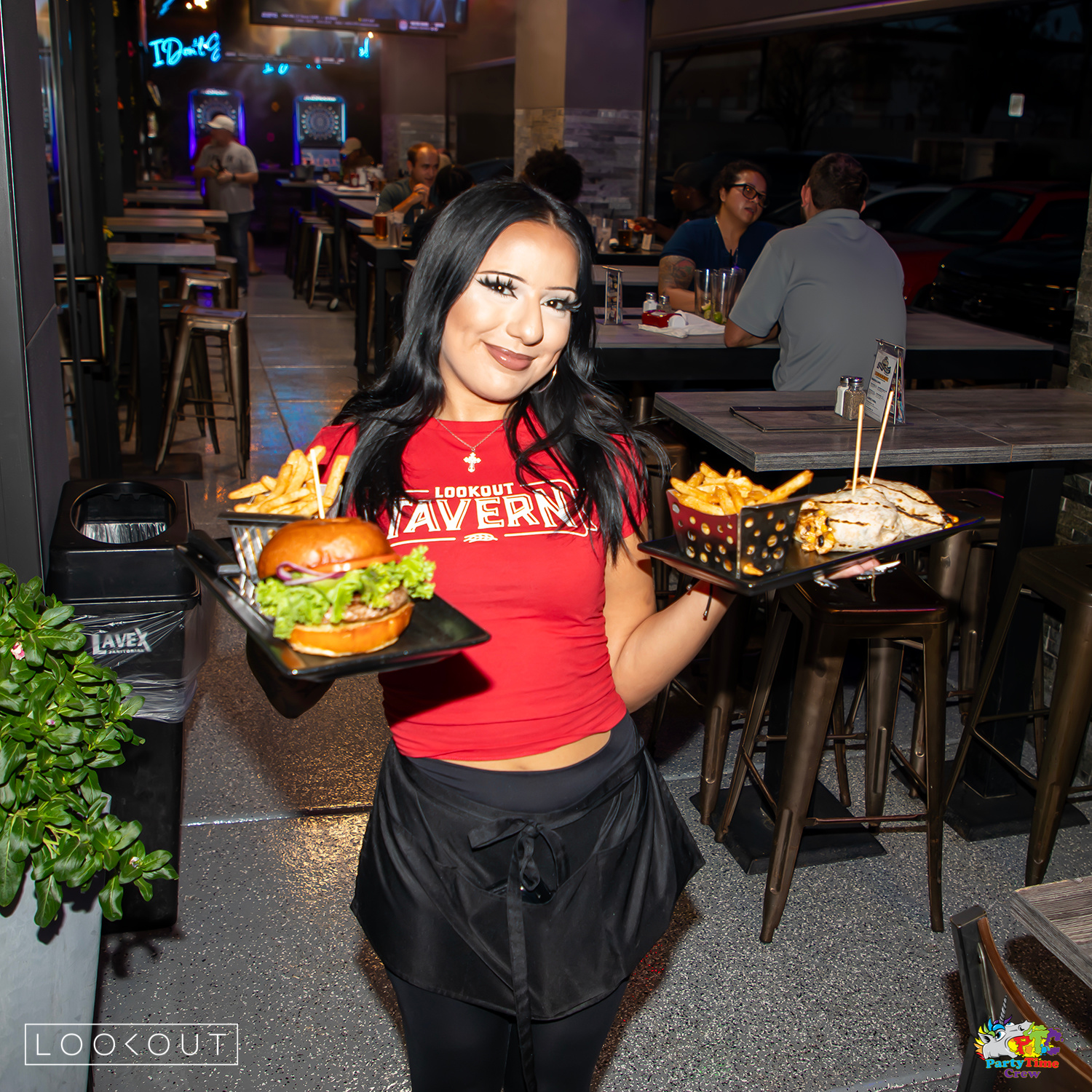 A server carrying a burger and a wrap with fries across the patio