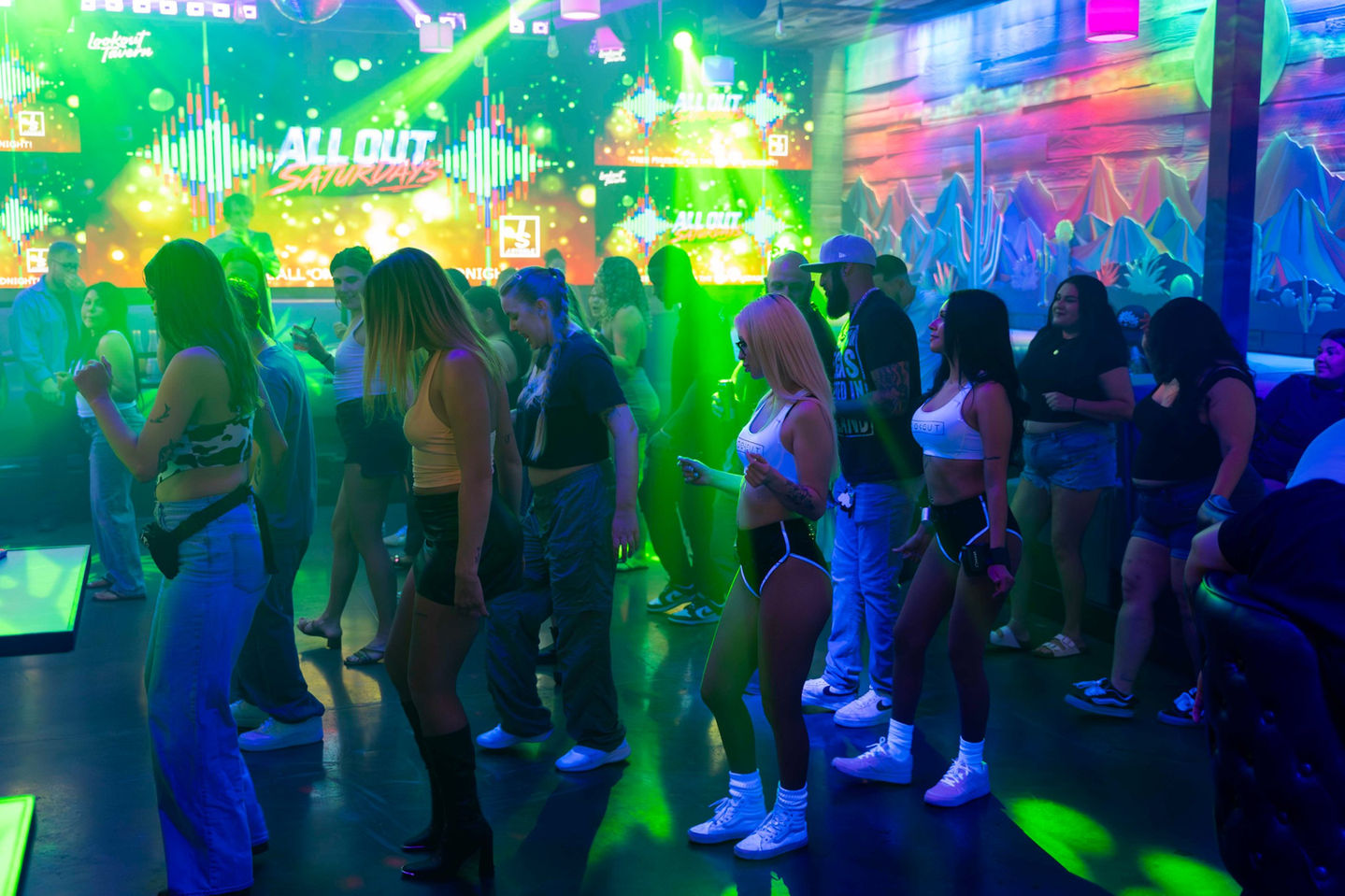 A packed dance floor on an All Out Saturday at Lookout Tavern, the LED walls and club lights overhead and the desert mural on the right
