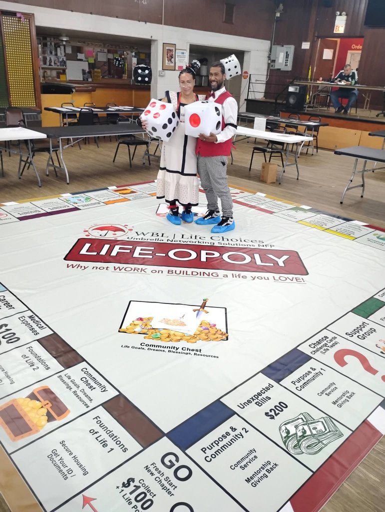Two players standing on the WBL Life-Opoly board holding large inflatable dice