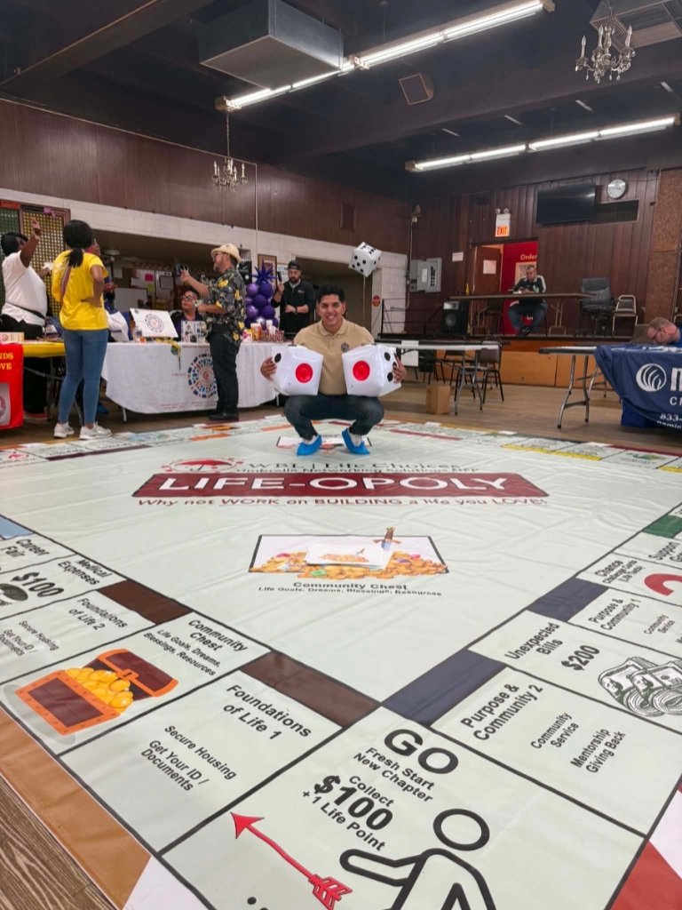 WBL LIFE-OPOLY floor board game with a participant crouching and holding giant foam dice
