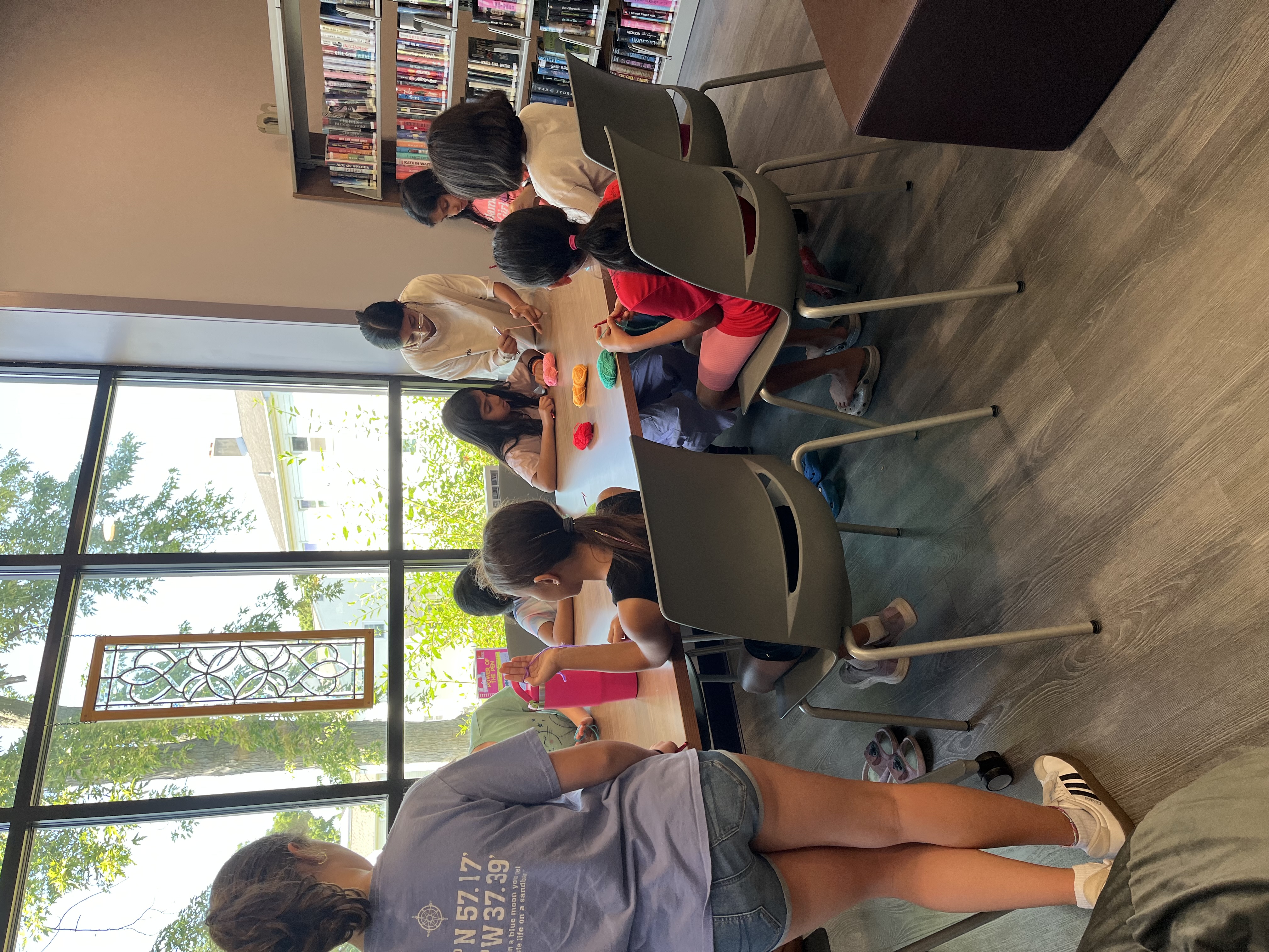 A crochet circle at a library table by the window, work in progress in everyone's hands.