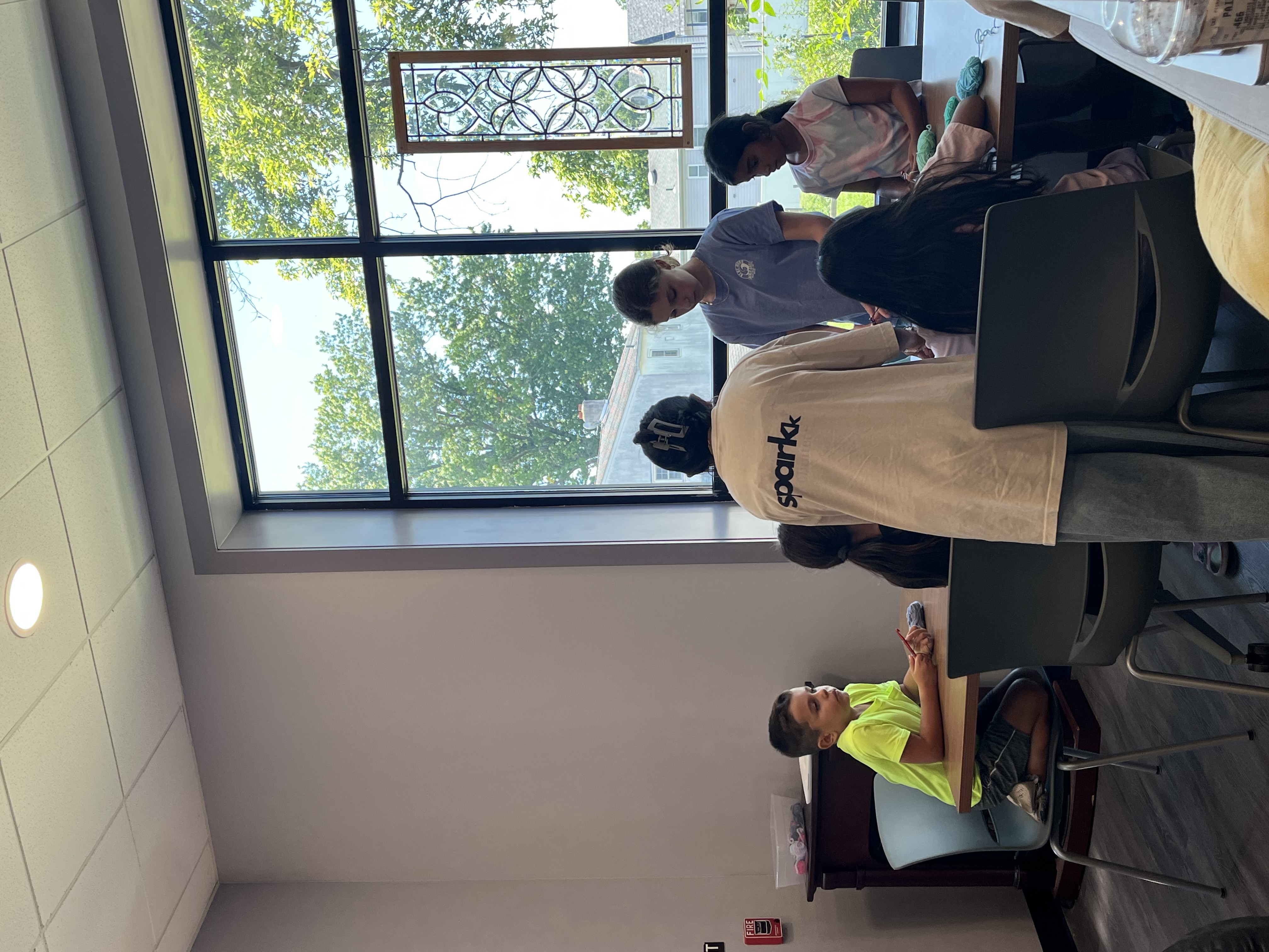 Crochet being taught around a library table beside a tall window.