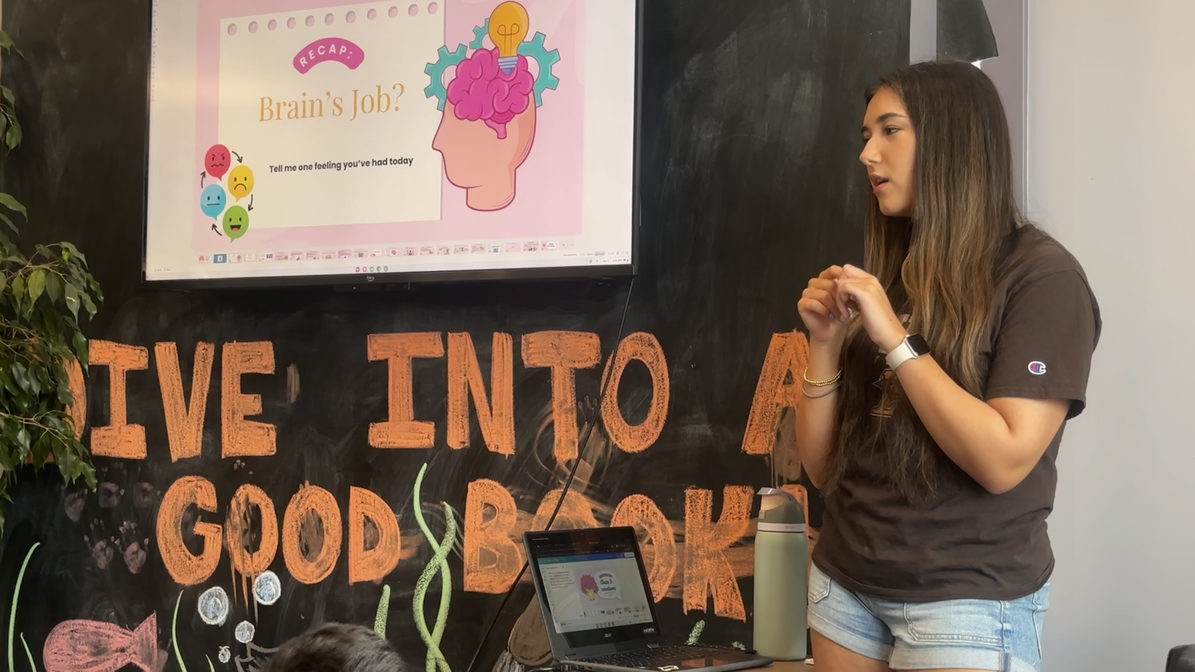 A psychology lesson being taught from the front of a library room, a slide about the brain on the screen behind.