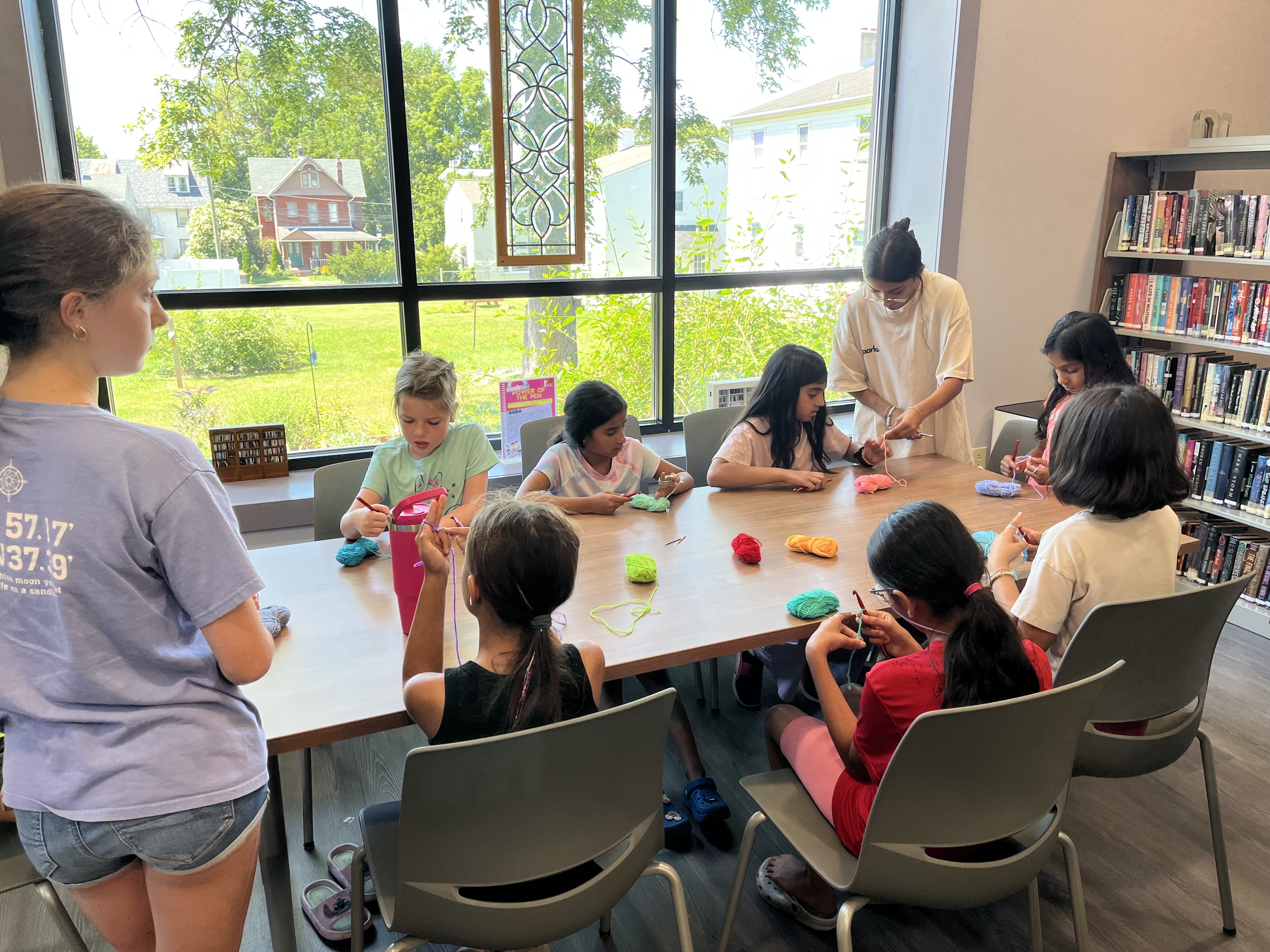 A crochet class working around a long library table, coloured yarn and hooks in use.