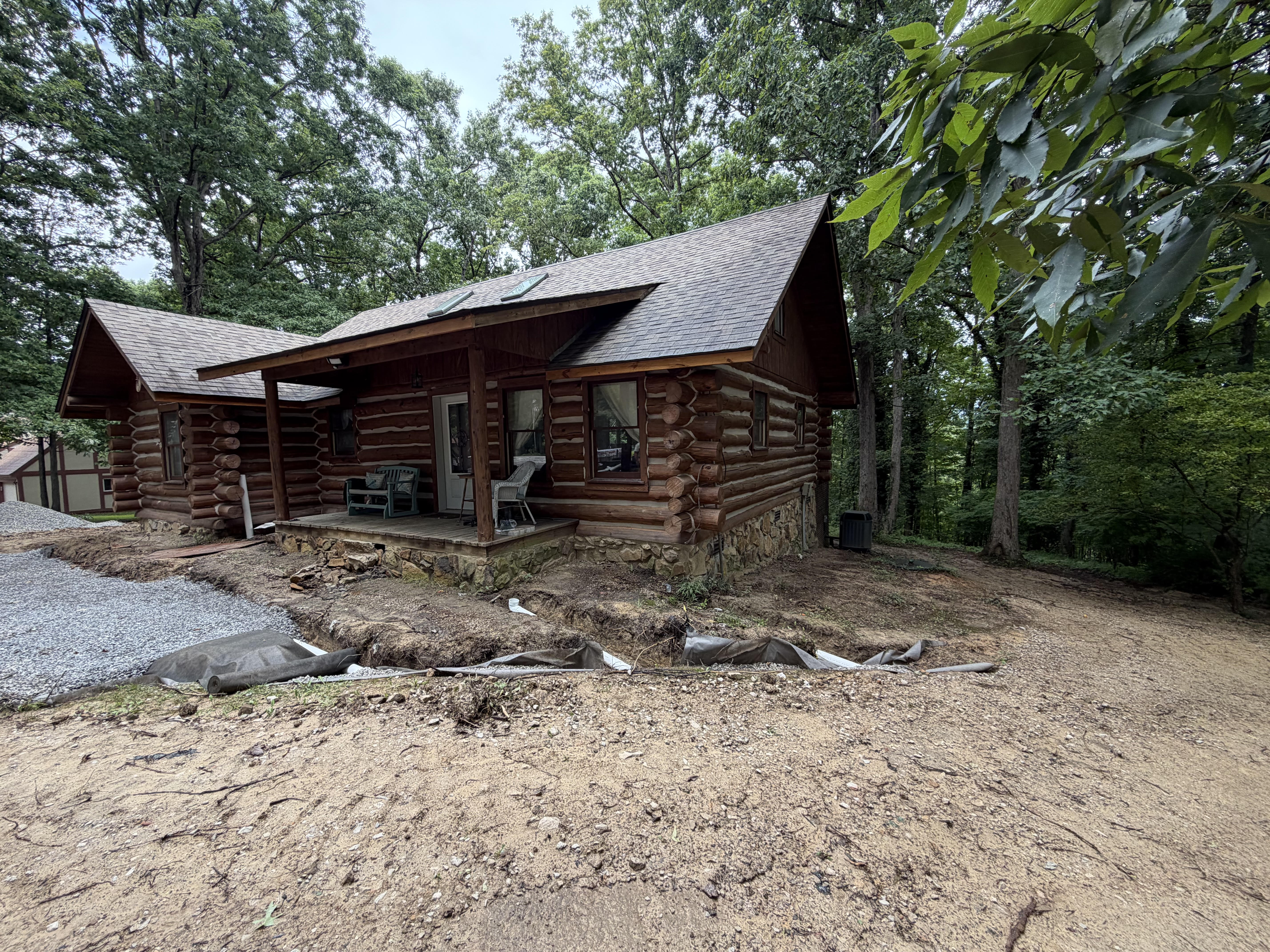 Excavated trench with drainage pipe and gravel beside a log cabin