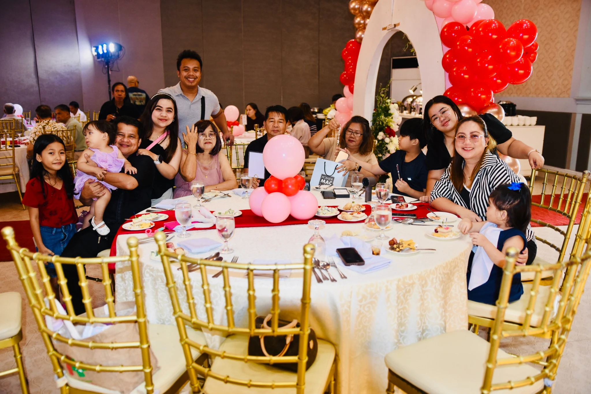 Adults and children smile and wave beside a reception table.