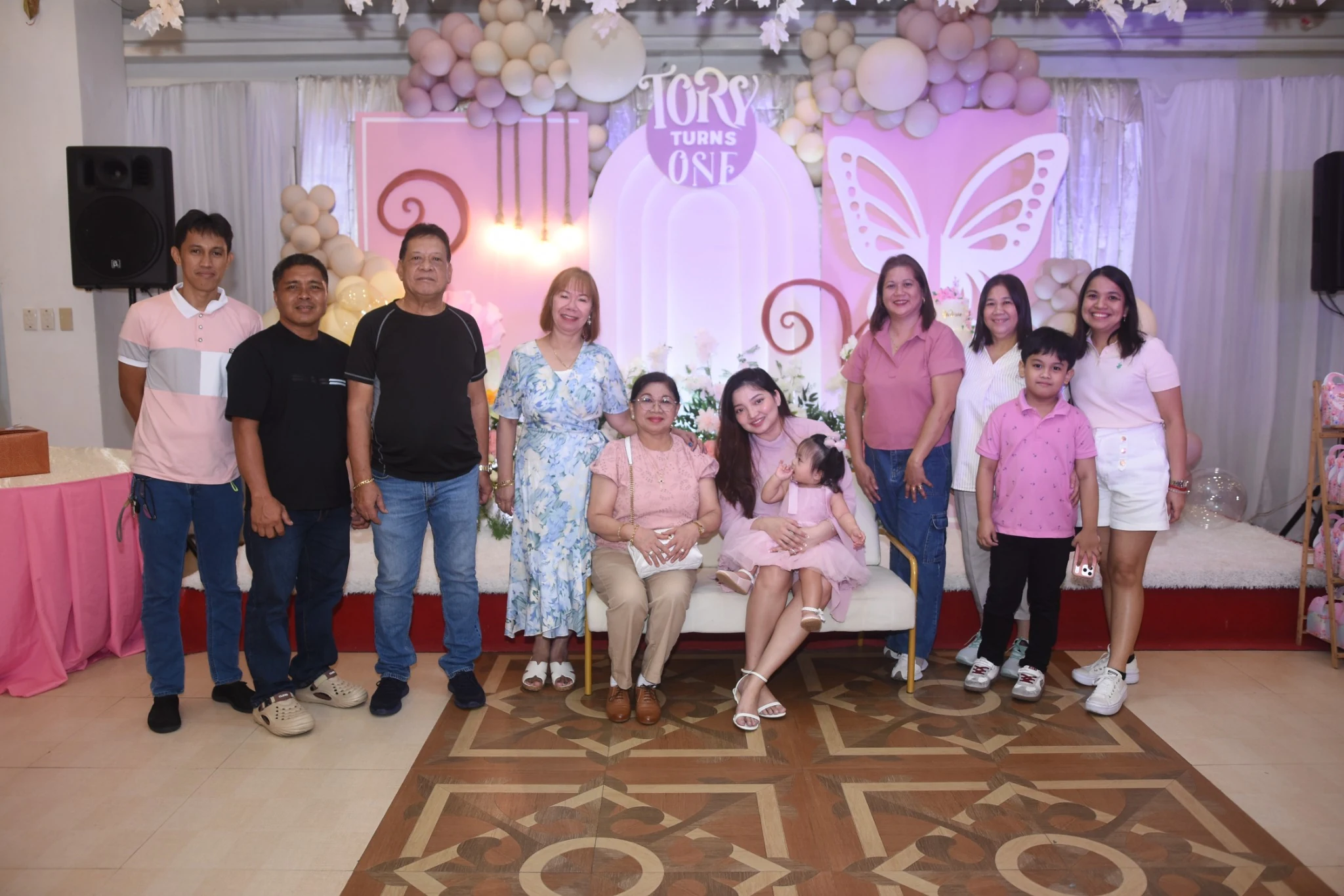Guests pose around a child in a pink dress at the first-birthday celebration.