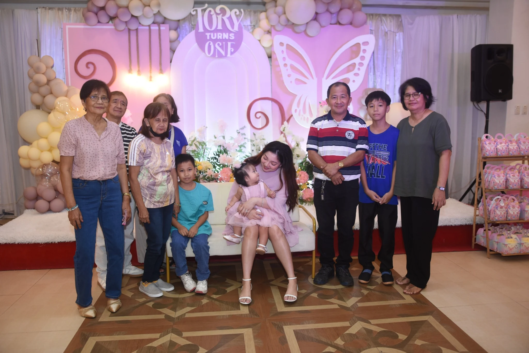 A seated adult looks down at the birthday child during a group photograph.