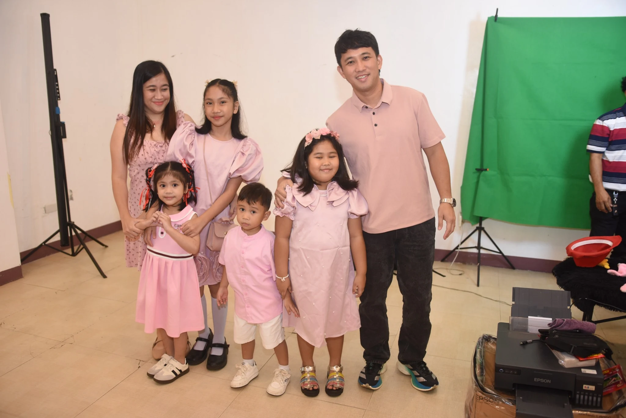 Two adults and four children in pink clothing pose beside a photo booth setup.