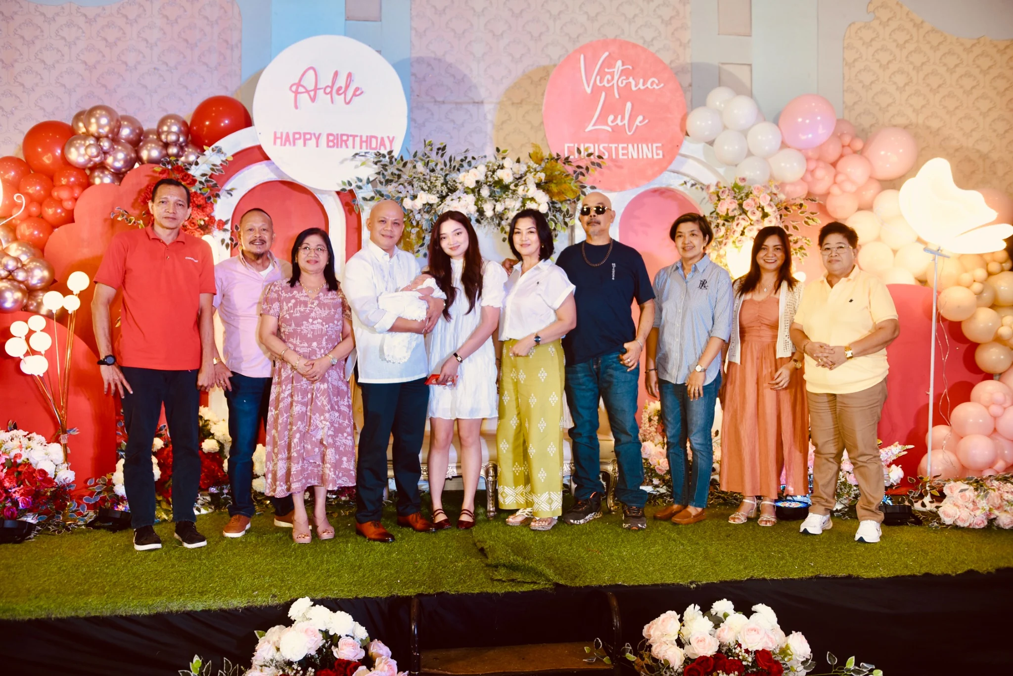 A group gathers with the baby for a portrait against the floral christening backdrop at the reception.